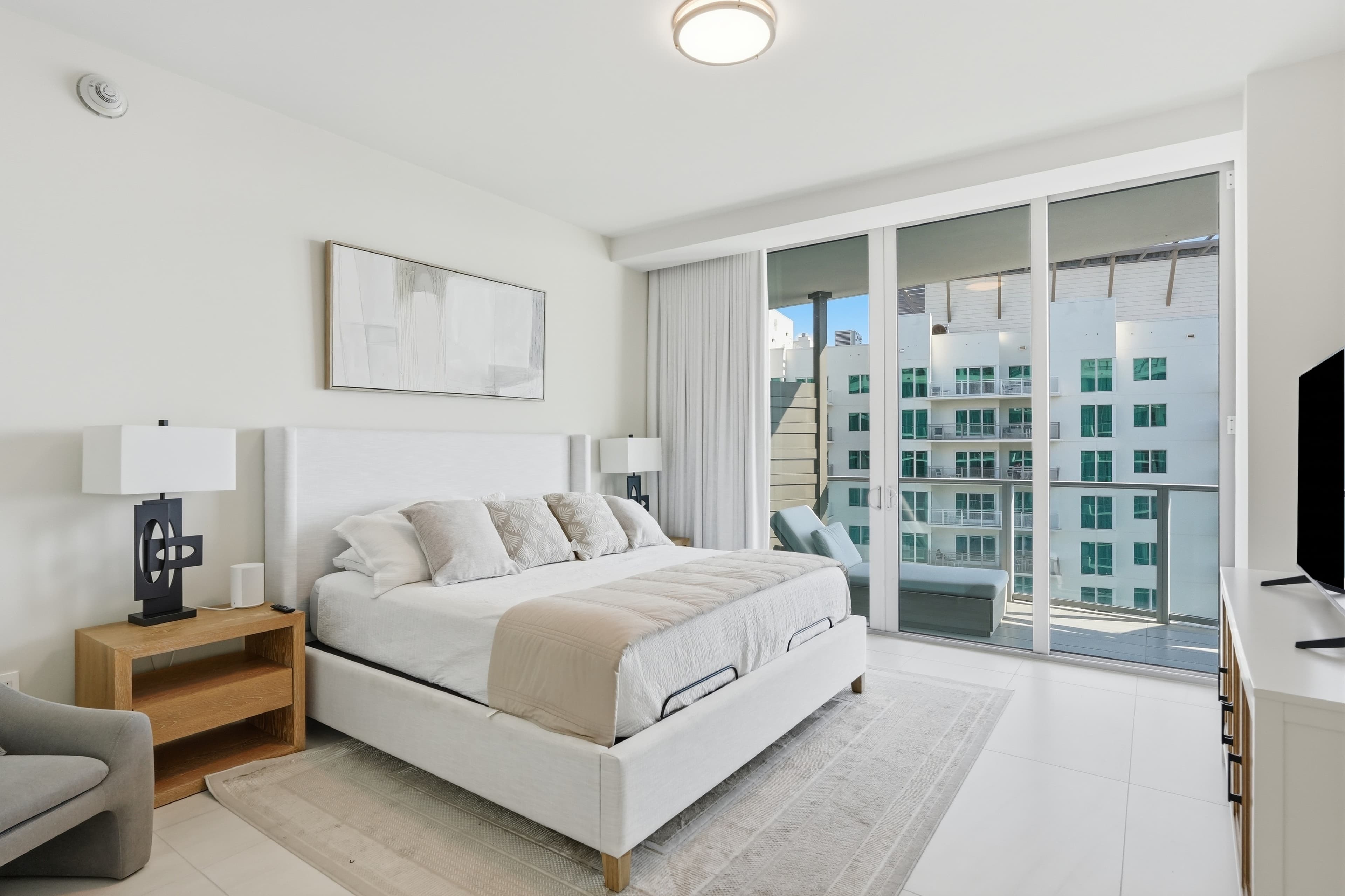Bedroom with white linens, balcony, and neighboring high-rise view
