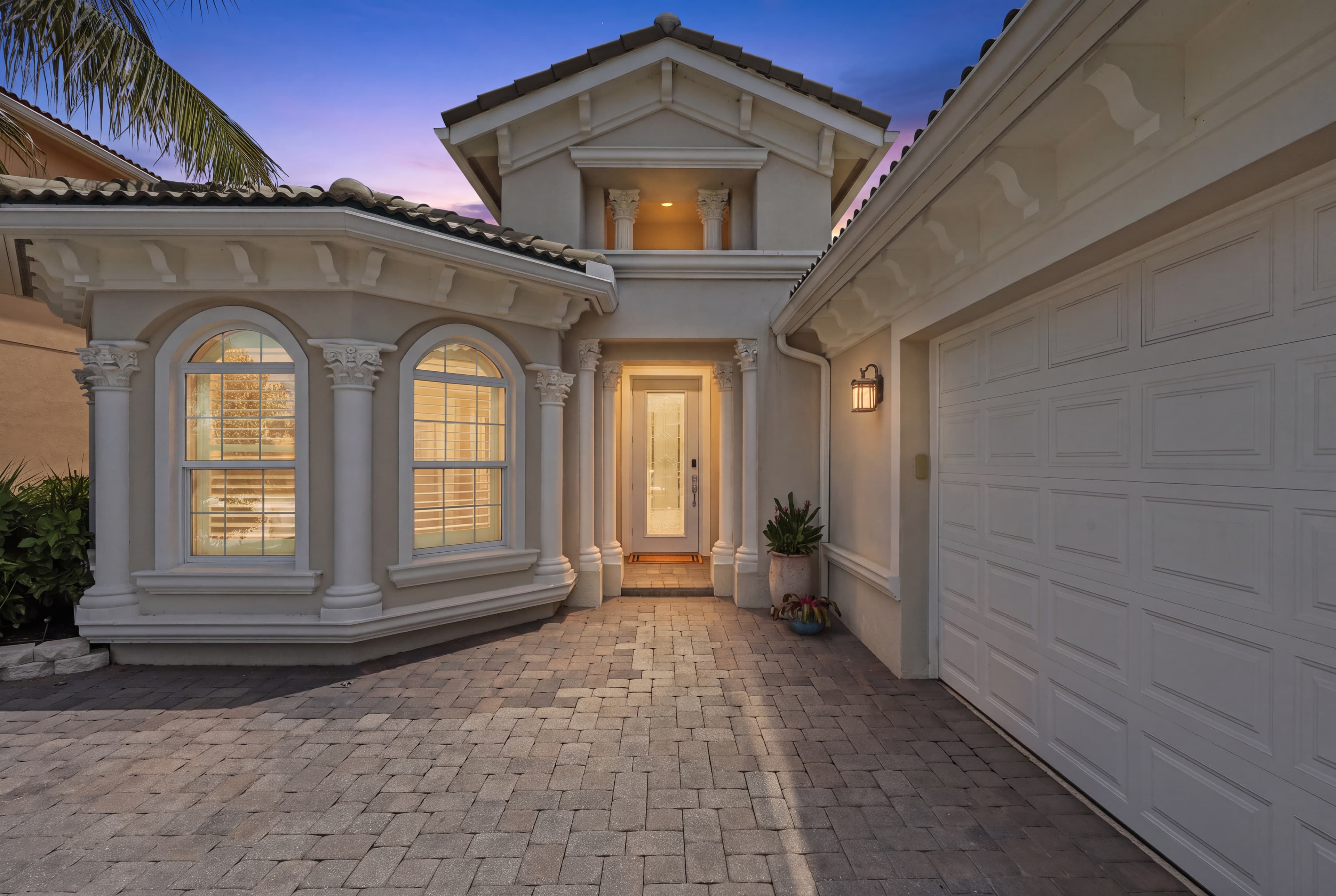 Illuminated Mediterranean entrance and paver driveway at twilight