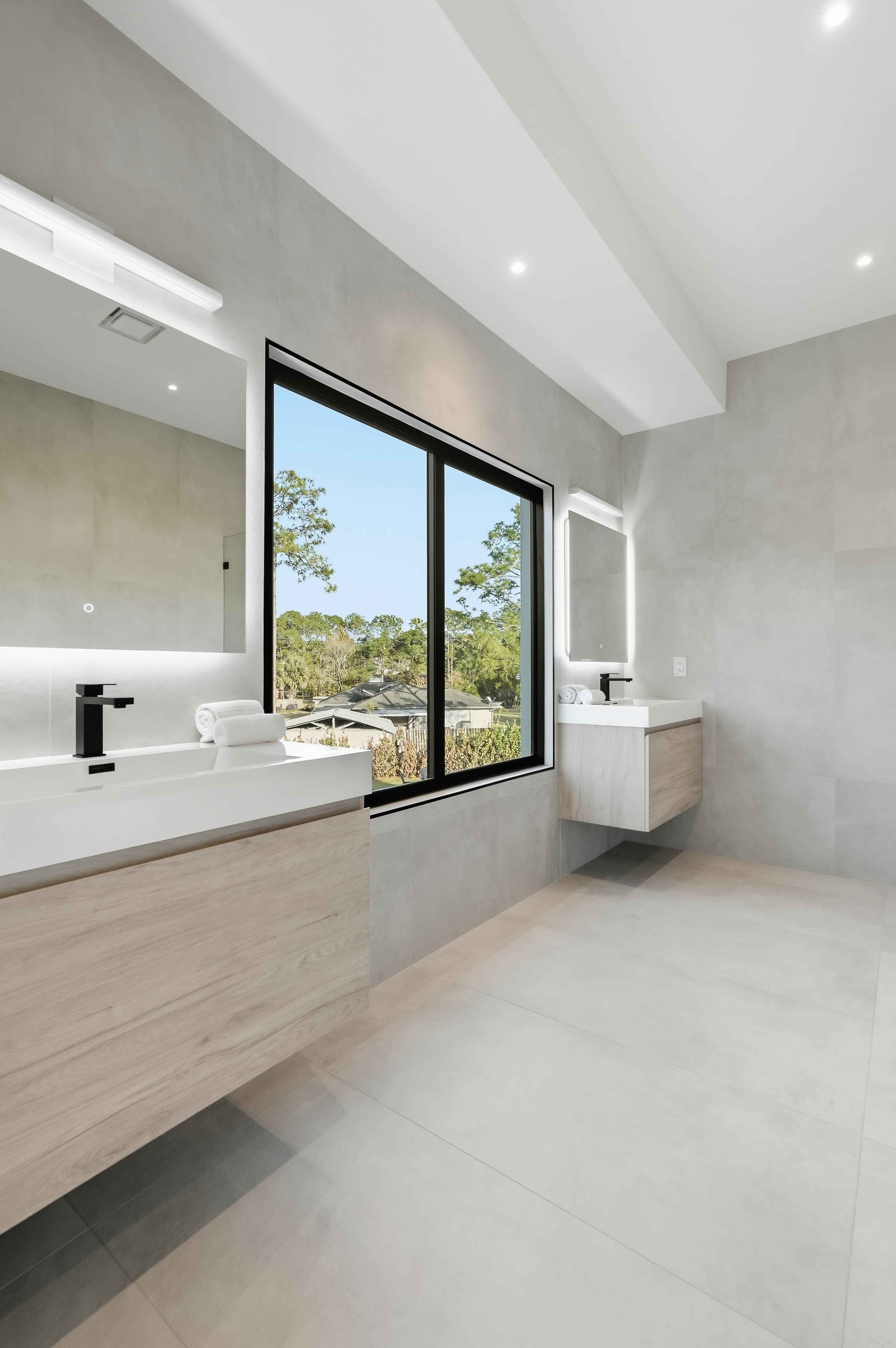 Modern bath with dual wood vanities, backlit mirrors, and a center window